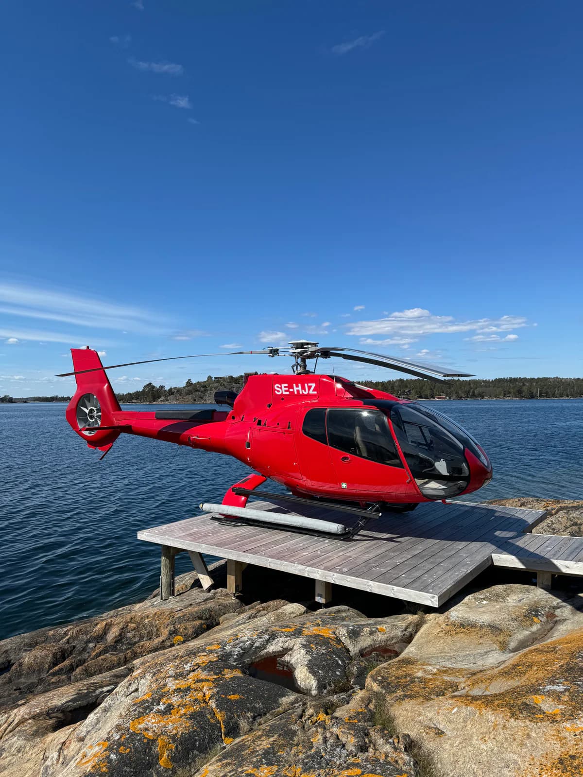 A red Airbus EC130 helicopter on a coastal helipad