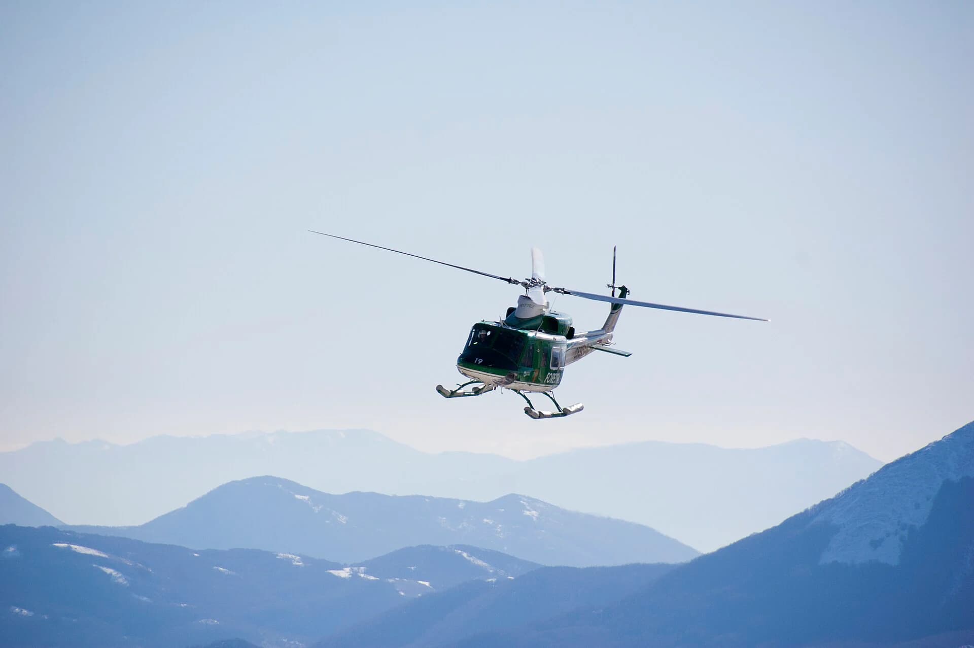 A Bell 412 approaching through a snow-covered mountain range