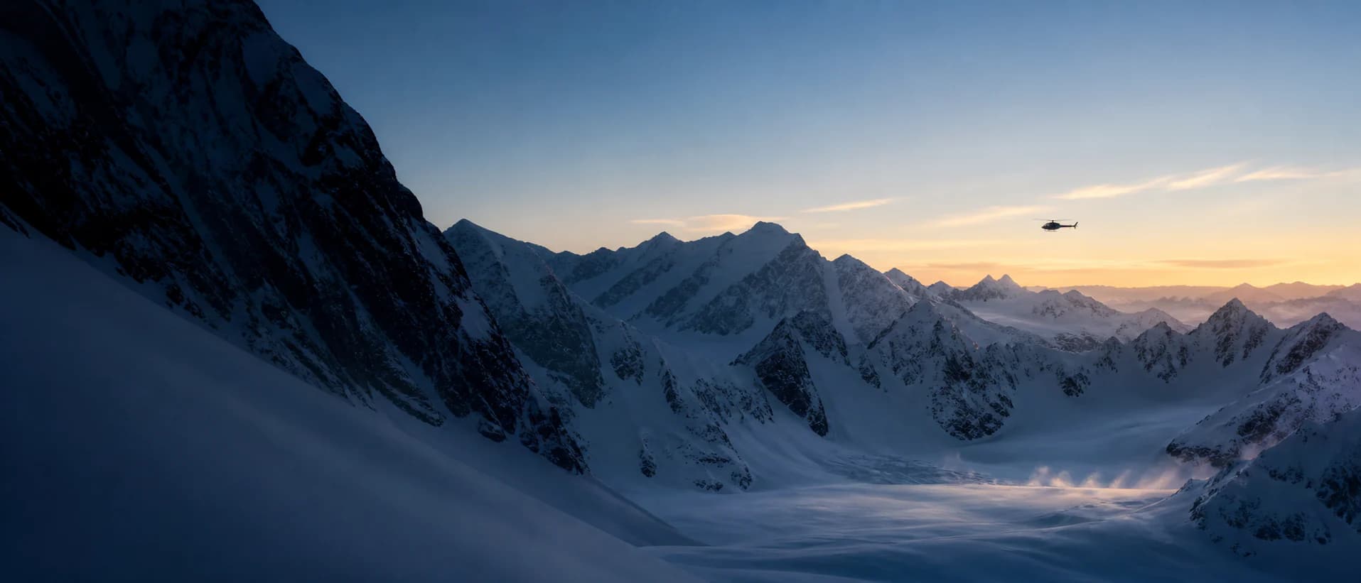 A distant helicopter crossing a glaciated mountain range at dawn