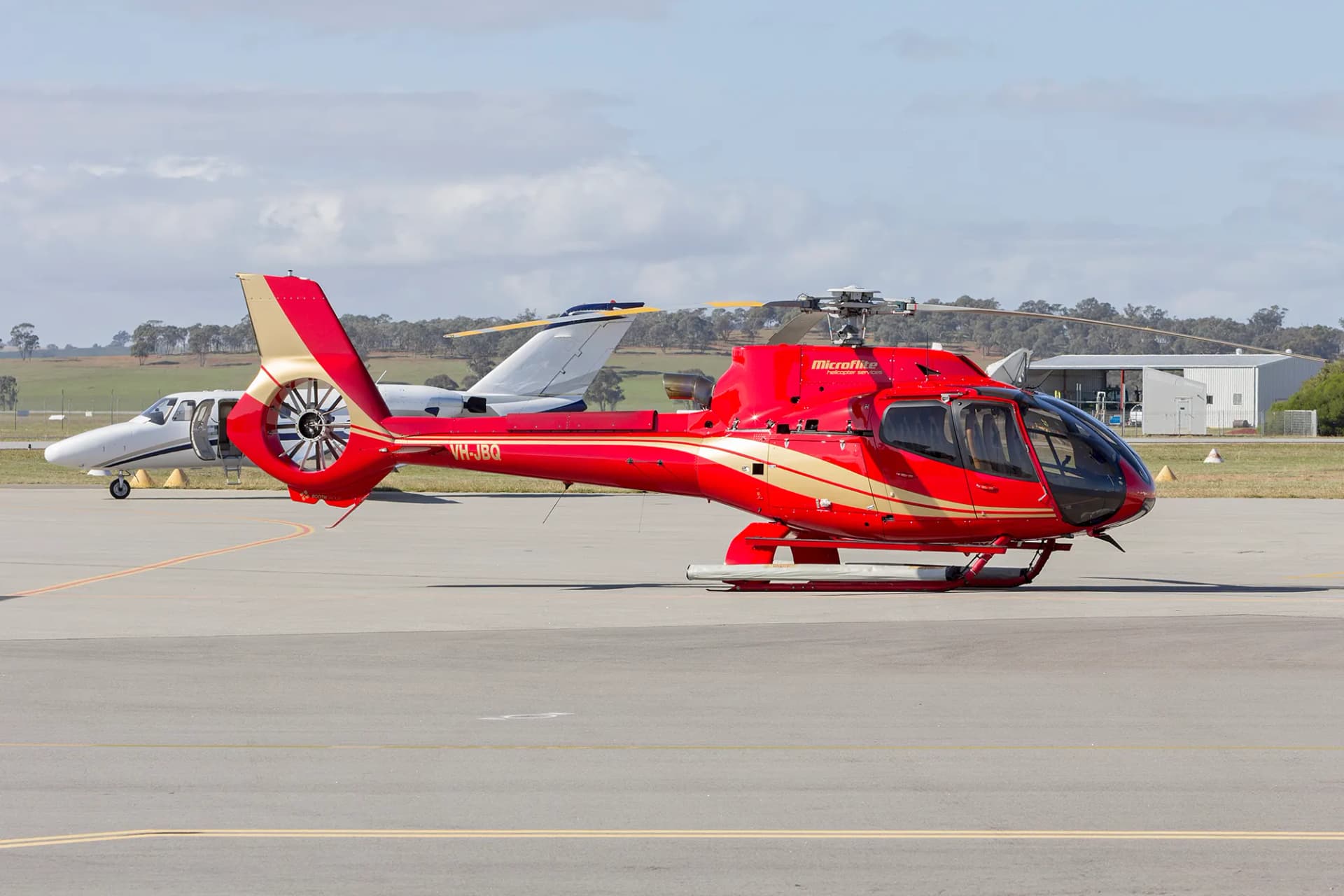 A red Airbus H130 parked on a helipad in daylight