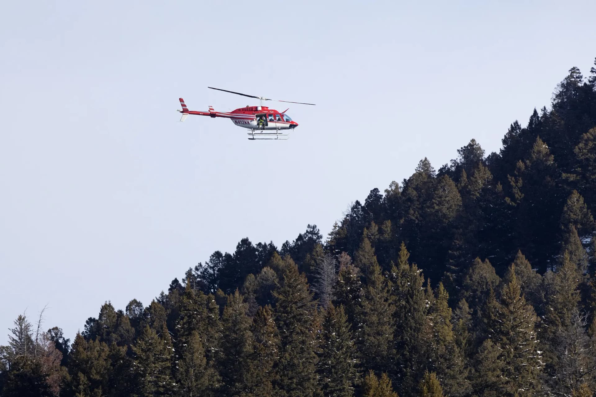 A Bell 206L LongRanger flying above a snowy mountain forest