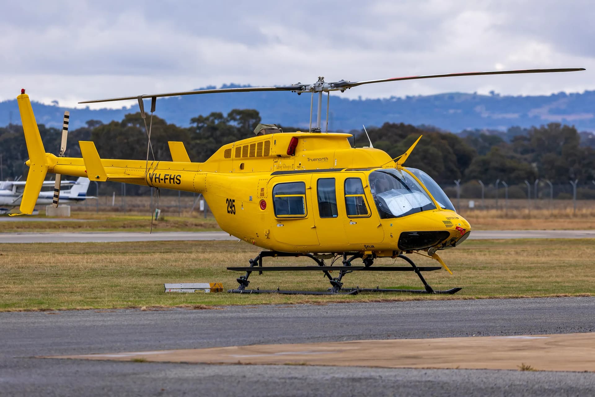 A yellow Bell 206L-4 LongRanger parked on an airport apron