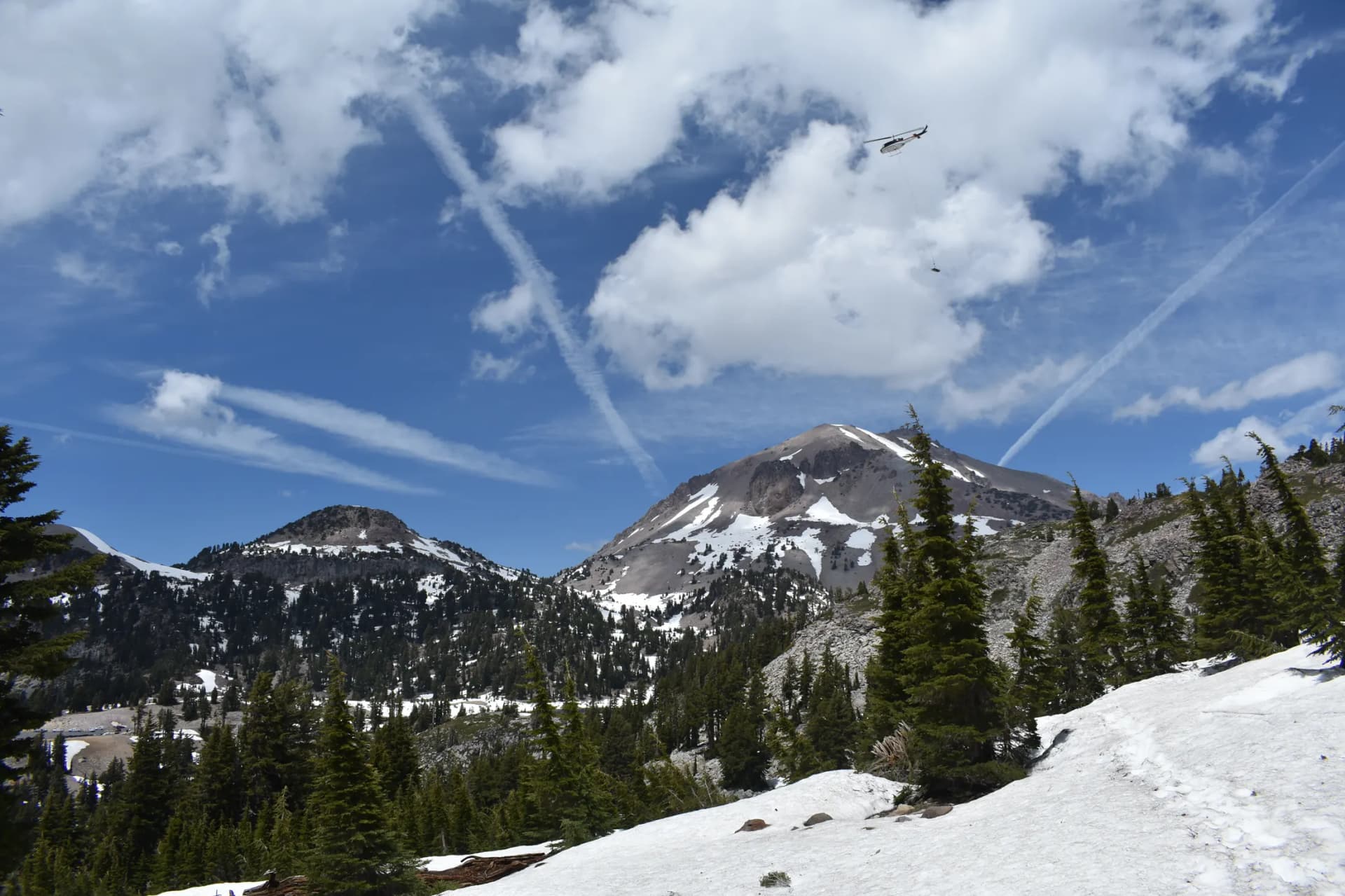 A Bell 205 carrying an external load above snow-covered Lassen Peak